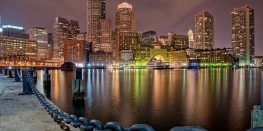Nighttime cityscape reflecting on calm water with a view from the waterfront.
