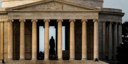 Silhouette of a person standing in the entrance of the Jefferson Memorial with columns in the foreground.